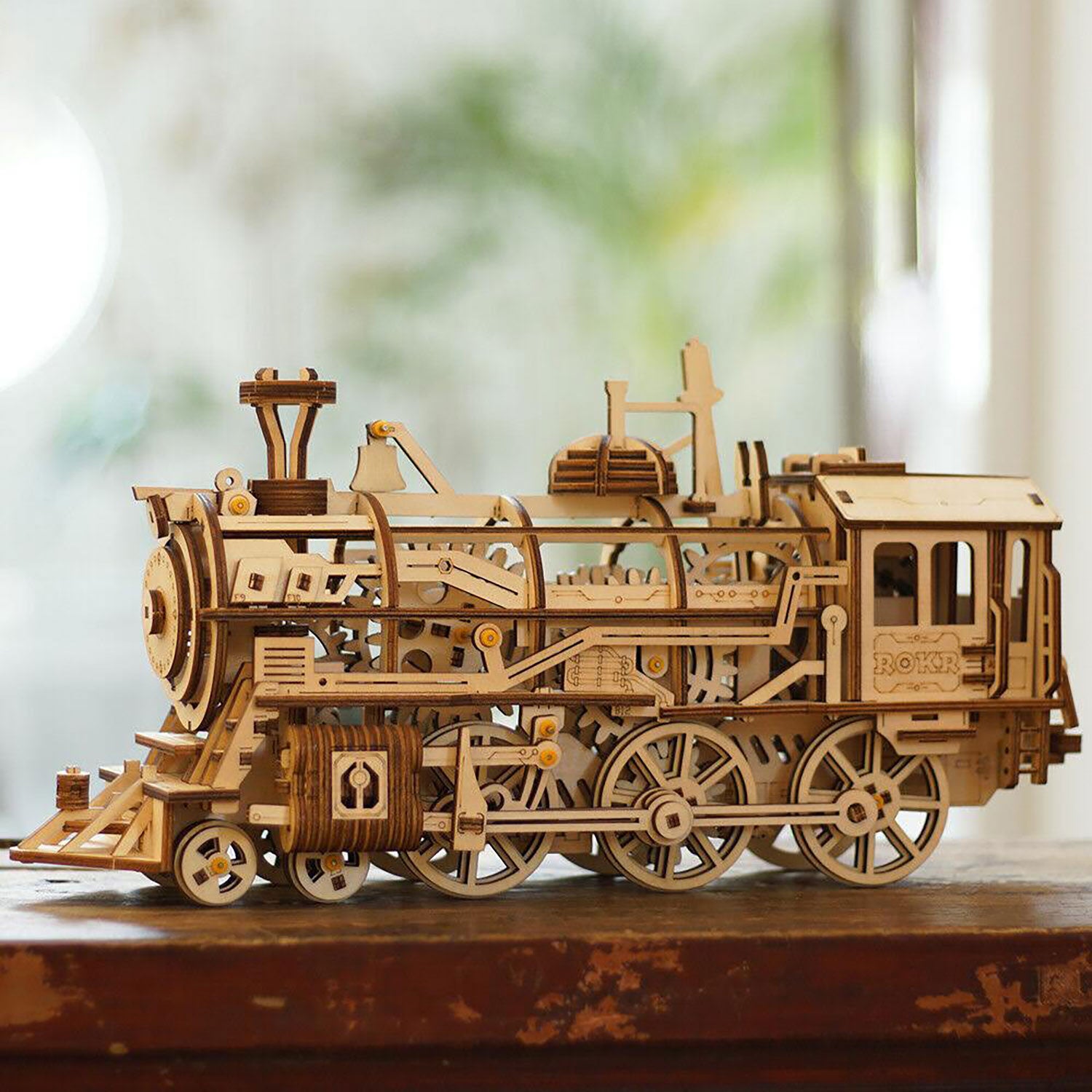 Das 3D-Holzpuzzle „Mechanische Dampf Express Eisenbahn“, ein detailliertes Holzmodell einer Dampflokomotive mit sichtbaren Zahnrädern und kleinen Komponenten, zeigt exquisite Handwerkskunst, während es auf einer Oberfläche vor einem leicht verschwommenen Hintergrund liegt.