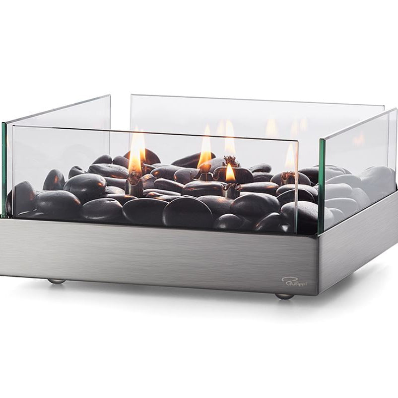 Design-Tischkamin mit schwarzen Steinen, Glaswänden und sichtbaren Flammen in einem modernen Edelstahl-Gehäuse. Für den Betrieb wird Paraffinöl verwendet.
