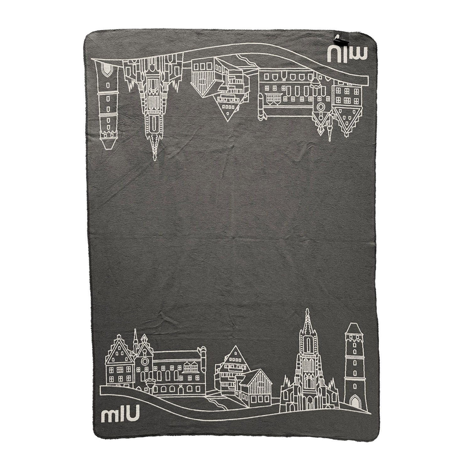 Die Kuscheldecke Ulm aus Baumwolle ist eine graue Decke mit weißen Linien, die an den Rändern architektonische Motive von Türmen und Gebäuden wie dem Ulmer Münster zeigen. In zwei Ecken ist das Wort „miu“ in Weiß zu sehen.