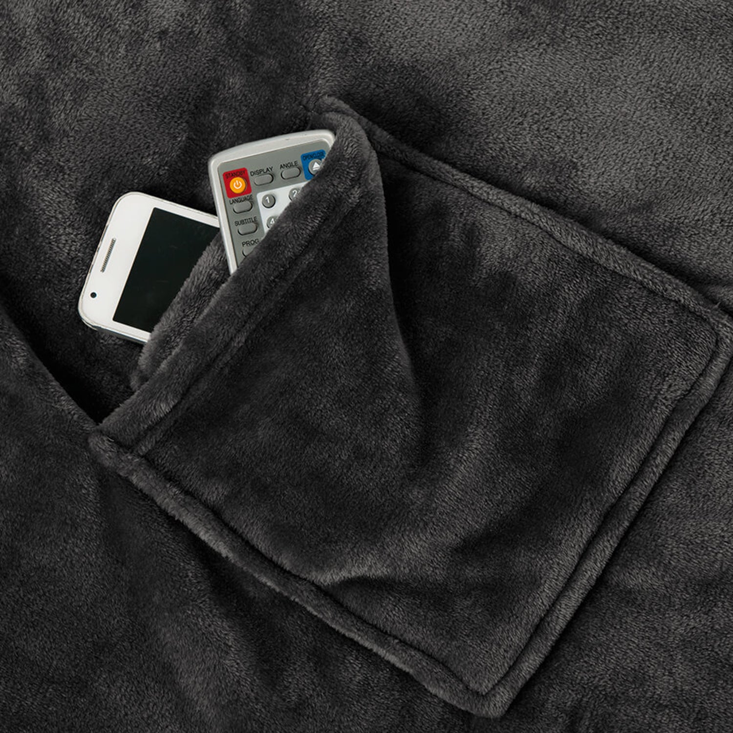 Eine dunkelgraue Kuscheldecke mit Ärmeln verfügt über eine offene Tasche, in der sich ein weißes Smartphone samt Fernbedienung befindet. Das nach Öko-Tex Standard 100 zertifizierte Material wirkt unglaublich weich und plüschig.