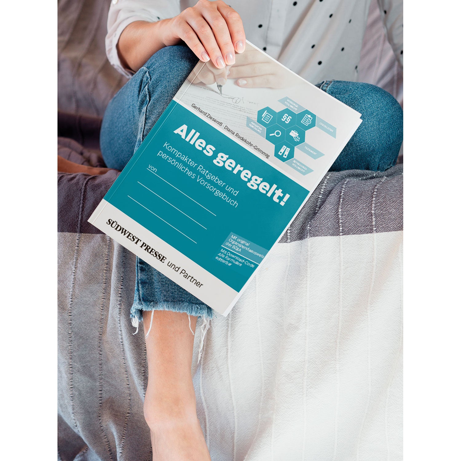 Eine Person sitzt mit übereinandergeschlagenen Beinen auf einer grauen Tagesdecke und hält das Vorsorgeheft „Alles geregelt!“ in der Hand. Das blaue Cover ist mit weißem Text und Illustrationen zu den Themen Finanzen, Planung und Recht versehen. Sie trägt Jeans und liest die Zeitschrift.