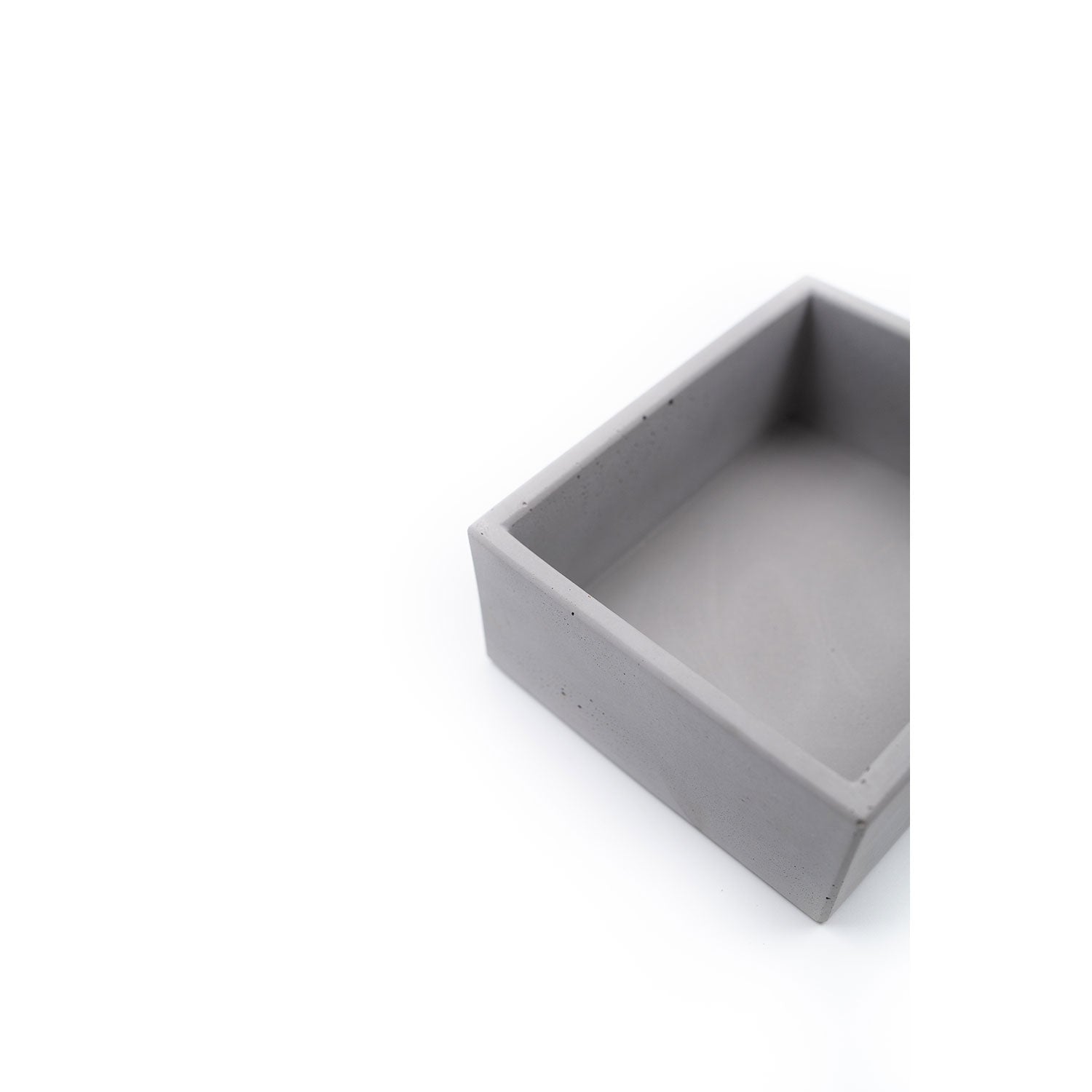 Eine minimalistische Aufbewahrungsbox mit Eichenholzdeckel aus grauem Beton steht vor einem weißen Hintergrund. Nur eine Ecke ist sichtbar, was die klaren Linien und die glatte Textur hervorhebt.