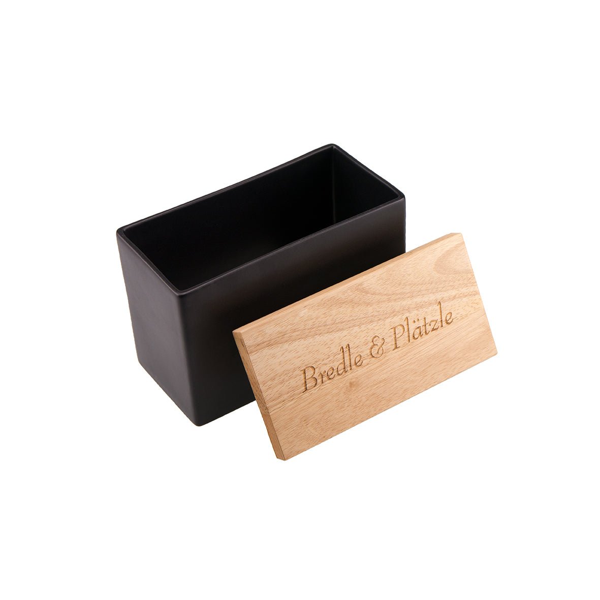 Die Keksdose aus Keramik ist eine schwarze, rechteckige Keramikdose mit offenem Deckel. Daneben befindet sich ein Holzdeckel mit der eleganten Lasergravur „Bredle & Plätzle“ auf schlichtem, weißem Hintergrund.