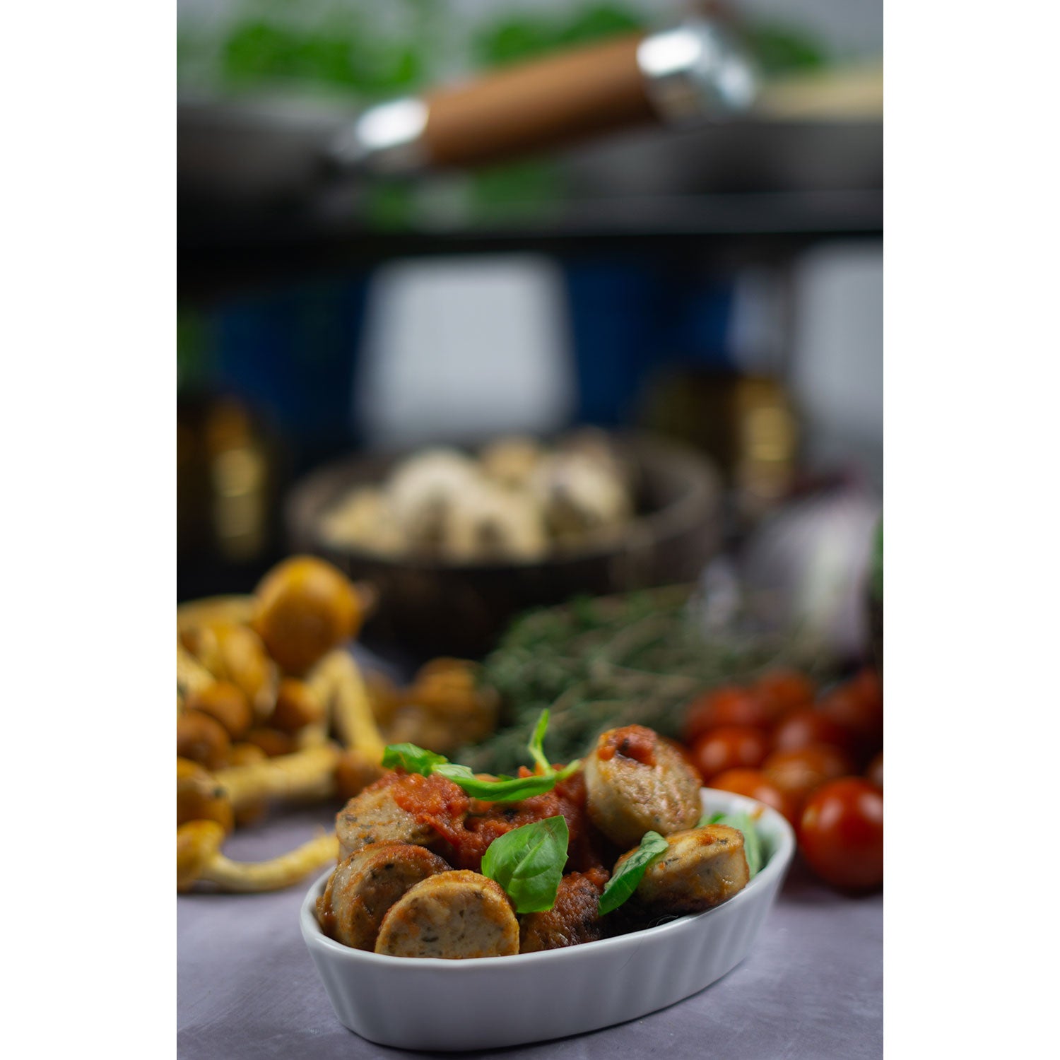 Ein weißer Teller gefüllt mit Wurstscheiben, garniert mit Tomatensauce und frischem Basilikum, sorgt für einen wahren Soulfood-Moment. Im Hintergrund zieren verschiedene Pilze, Kirschtomaten und Kräuter ein verschwommenes Küchenwerkzeug. Erleben Sie das mit DeWok. Das neue Kochsystem!.