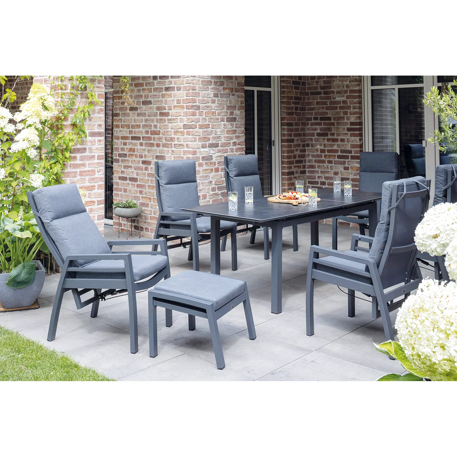 Das klappbare Gartenstuhl-Ess-Relaxsessel-Set Merida 2er besteht aus zwei klappbaren, gepolsterten Stühlen, die sich perfekt zum Entspannen rund um einen Esstisch auf einer Terrasse mit üppigen Pflanzen eignen – ideal für Zusammenkünfte im Freien mit Snacks und Getränken.