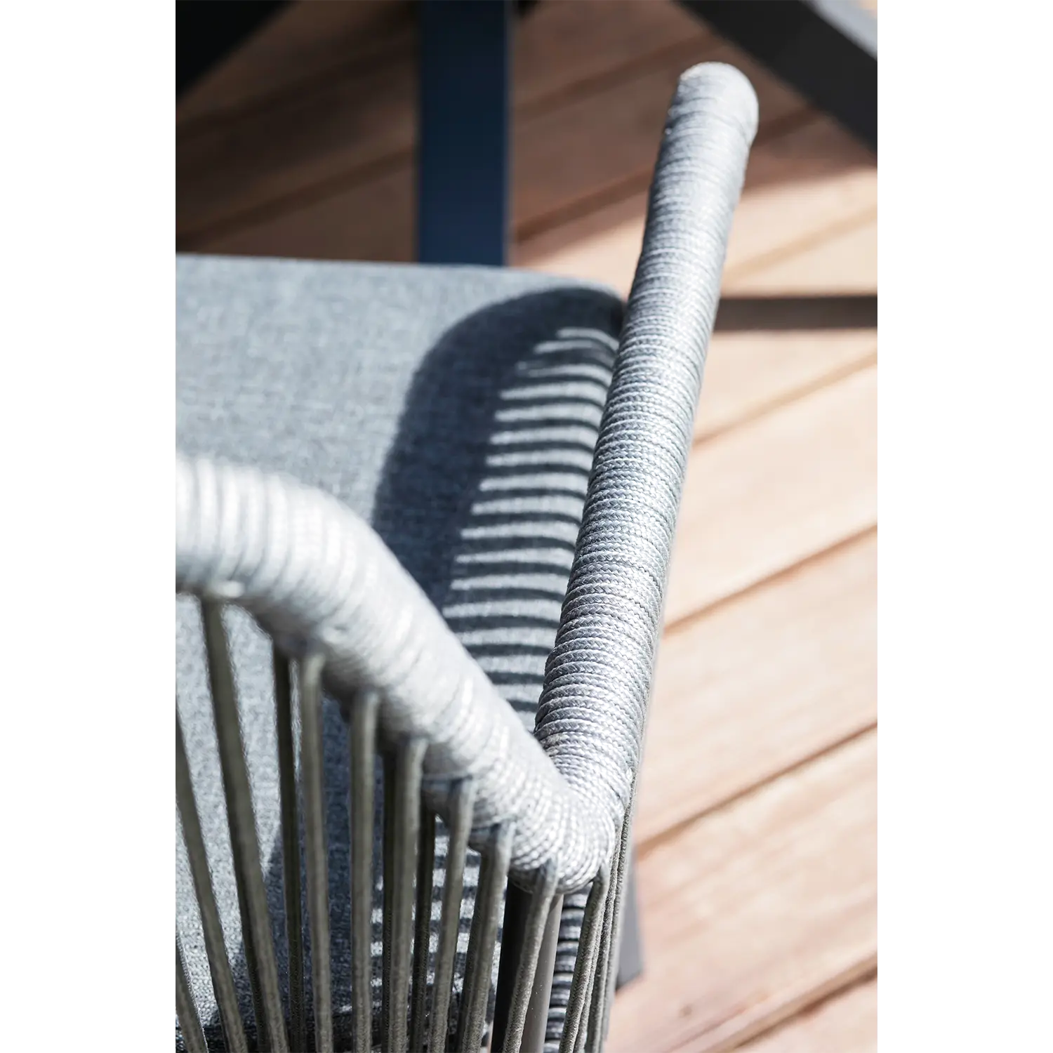Nahaufnahme eines eleganten Esszimmerstuhls Marbella Rope 2er-Sets mit grauen, seilumwickelten Armlehnen, die Schatten auf die Kissen werfen. Dieses wetterfeste Stuhlset ist ideal für den Außenbereich und steht stilvoll auf einer Holzterrasse, wo das Sonnenlicht mit Licht- und Schattenmustern interagiert.
