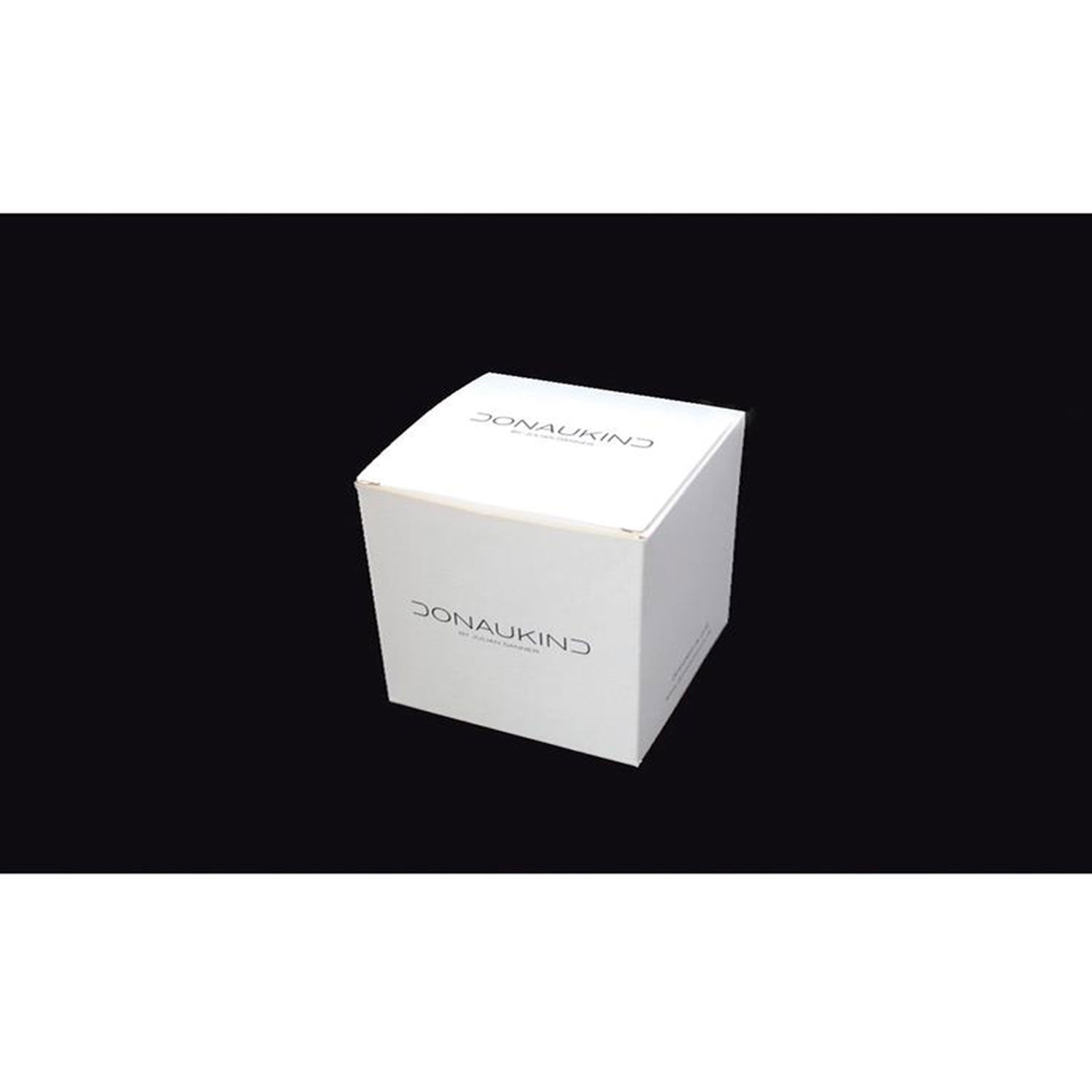 Eine weiße, würfelförmige Box mittig vor schwarzem Hintergrund zeigt elegant „Donaukind“ in minimalistischer Schriftart und weist damit auf die Qualität der Ulmer Wahrzeichen Tasse – „Ulmer Fischerstechen“ hin, die an feines Porzellandekor erinnert.