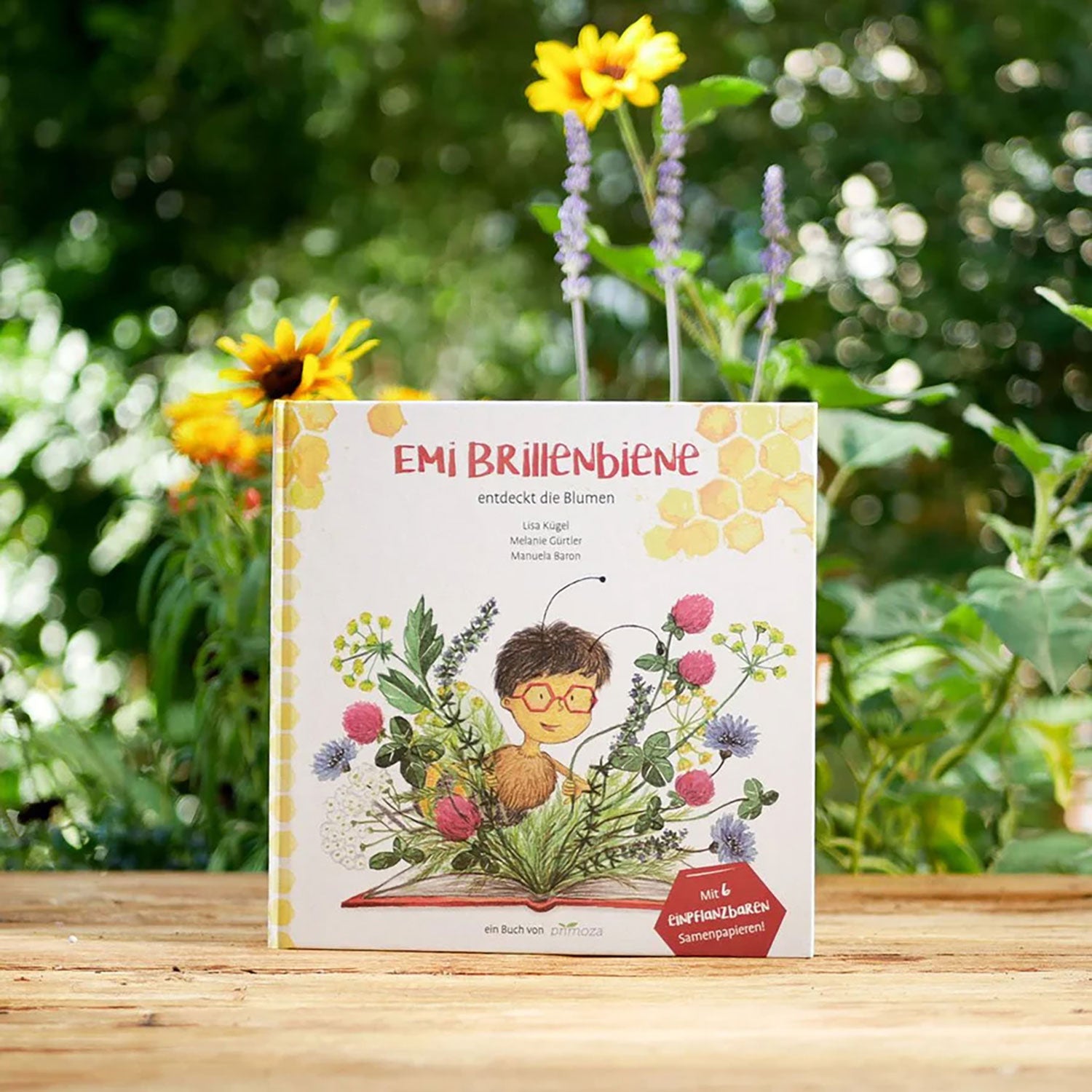 Ein Kinderbuch mit dem Titel „Emi Brillenbiene – Die weite Reise einer kleinen Biene“ steht aufrecht im Freien. Auf dem Cover ist ein Kind mit Brille abgebildet, umgeben von Bienen und Blumen vor verschwommenem Grün und gelben Blüten.