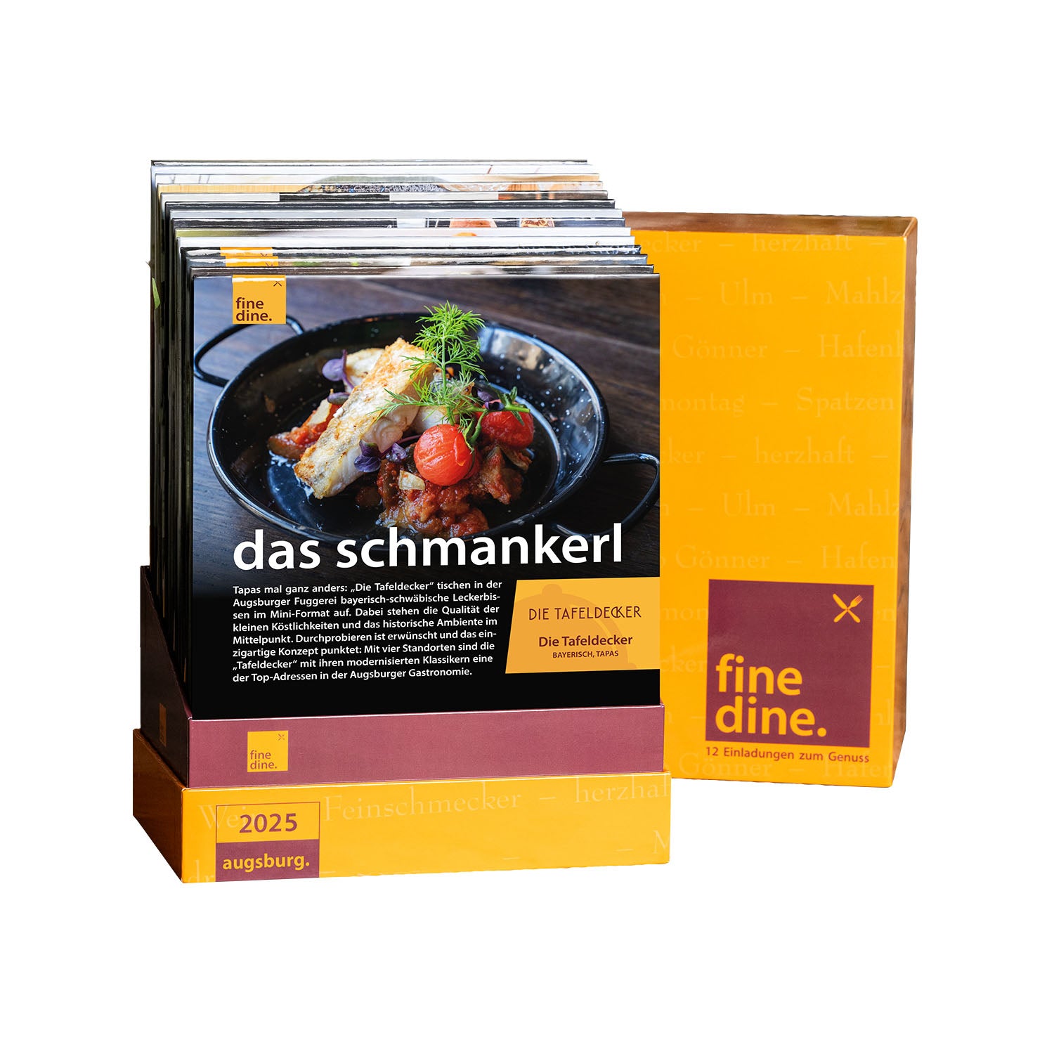 Die „Fine Dine Box Augsburg 2025“ besteht aus zwei Heften mit dem Titel „das schmankerl“, die jeweils ein Gericht mit Fleisch, Tomaten und Garnitur präsentieren. Die gelbe Box mit orangefarbenen Akzenten enthält 12 Restaurantgutscheine für kulinarische Erlebnisse in Augsburg 2025.