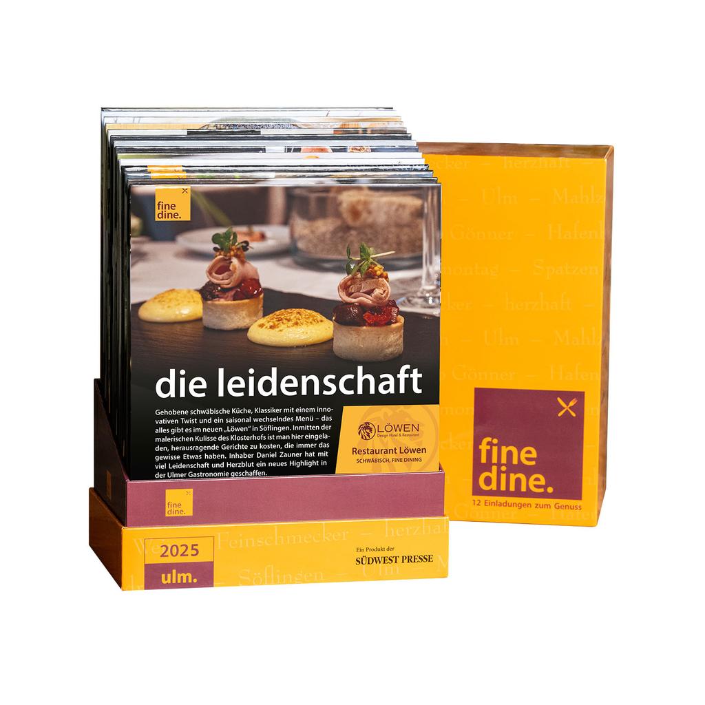 Die Fine Dine Box Ulm 2025 enthält die Karten „Die Leidenschaft“ mit einem Gourmet-Coverbild, darunter kleine Gebäck- und Fleischgerichte. Die Verpackung ist überwiegend gelb und schwarz gehalten und trägt einen eleganten Text mit dem Titel „Restaurantgutscheine Ulm“.