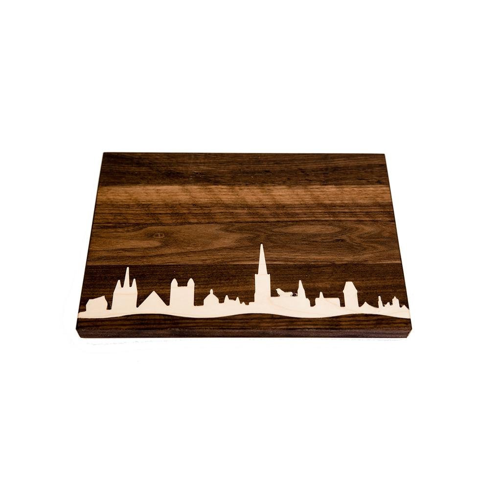 Das Frühstücks- oder Vesperbrettchen - dunkel besticht durch seine meisterhafte Verarbeitung und die dunkle Nussbaummaserung mit eleganter weißer Skyline-Einlage, die den Charme einer Stadtlandschaft einfängt.