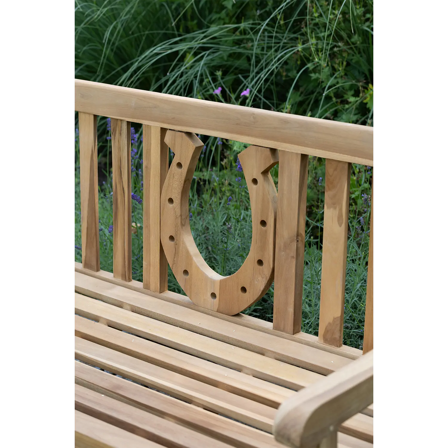 Die Teak-Gartenbank Hufeisen besticht durch ihre Lattenrückenlehne und Sitzfläche mit elegantem Hufeisenmotiv und eignet sich als vielseitige Sitzgelegenheit für drinnen und draußen. Sie wertet jeden Außenbereich perfekt auf, insbesondere vor üppigem Grün und Gras.