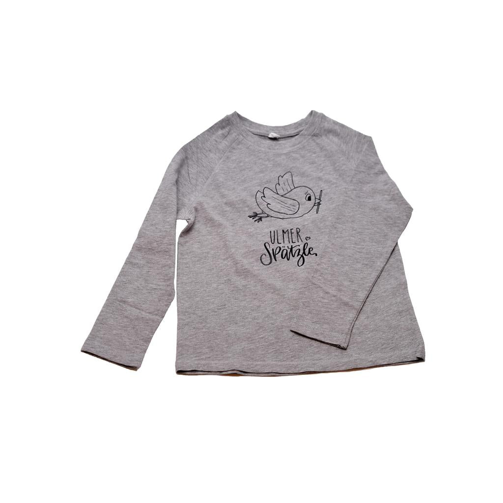 Das „Ulmer Spätzle“-Shirt für 4- bis 5-Jährige besticht durch ein hellgraues Design mit einer schlichten Vogelillustration und handgeschriebenem Text auf der Vorderseite, flach auf weißem Hintergrund dargestellt.