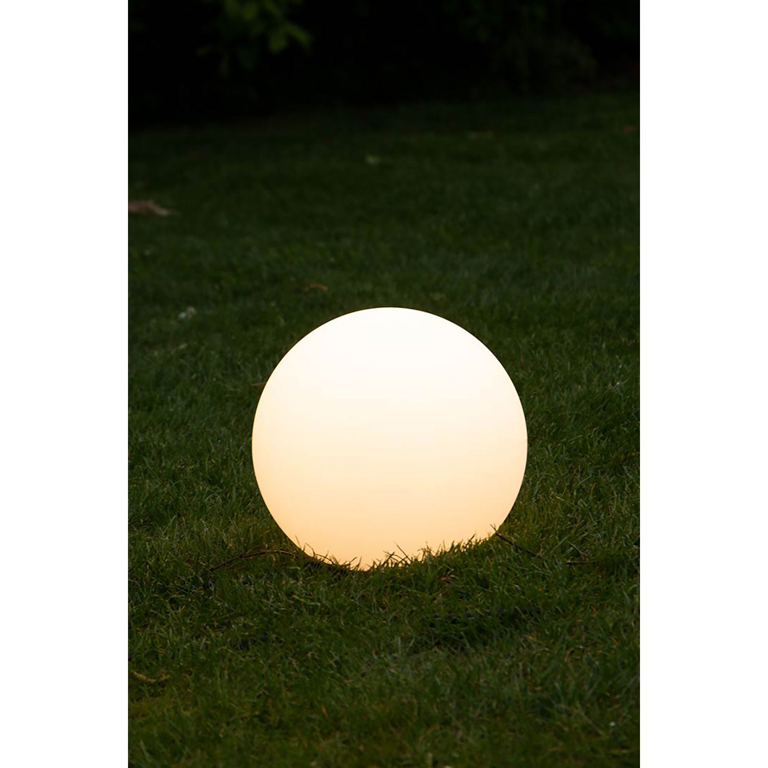 Eine leuchtende Solar-Leuchtkugel schmückt in der Dämmerung einen Rasen. Sie strahlt ein sanftes, warmes Licht aus und beleuchtet sanft das umgebende Gras, während der dunkle Hintergrund ihre umweltfreundliche Leuchtkraft unterstreicht.