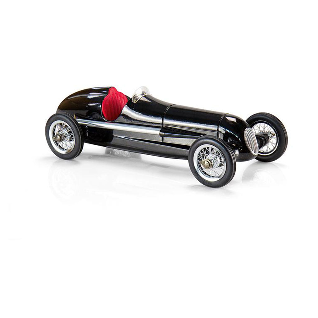 Das Modellauto „Silberpfeil“ (Schwarz) ist ein elegantes schwarzes Spielzeug-Rennauto im Vintage-Stil mit glänzenden silbernen Akzenten, einem leuchtend roten Sitz und aufwendig gestalteten Speichenrädern, die sich elegant auf einer glatten, reflektierenden weißen Oberfläche präsentieren.