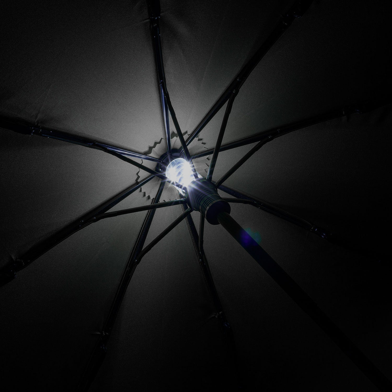Unter dem übergroßen Taschenschirm mit Beleuchtung enthüllt ein integriertes LED-Licht ein sternförmiges Muster aus Schirmrippen und Stoff vor dem dunklen Hintergrund, das durch sein Windproof-System noch verstärkt wird.