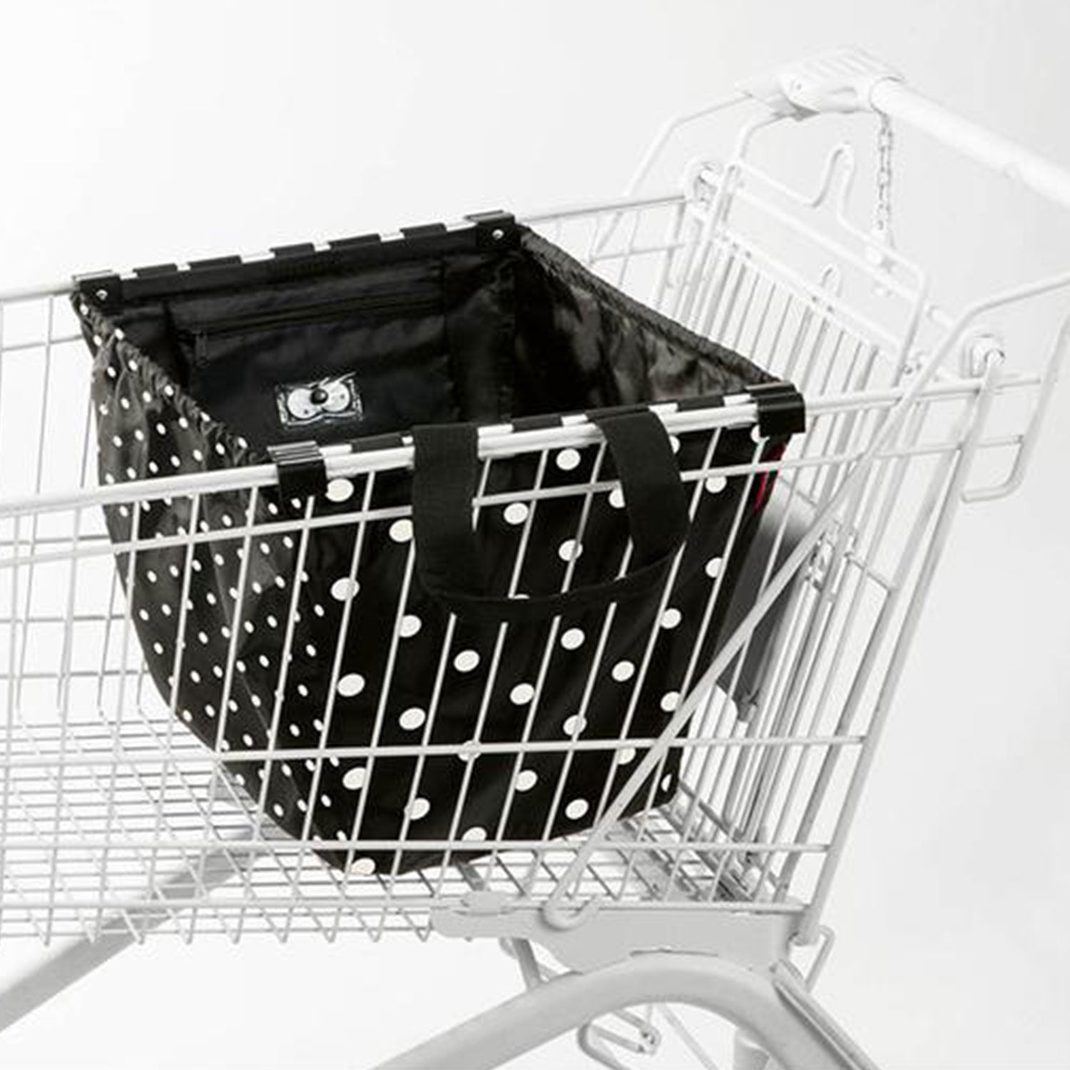 Die Reisenthel Easyshoppingbag dots mit ihrem schicken schwarz-weißen Punkte-Design präsentiert sich elegant im leeren Einkaufswagen vor weißem Hintergrund. Sie ist eine stilvolle und umweltfreundliche Wahl für alle, die einen nachhaltigen Lebensstil pflegen.