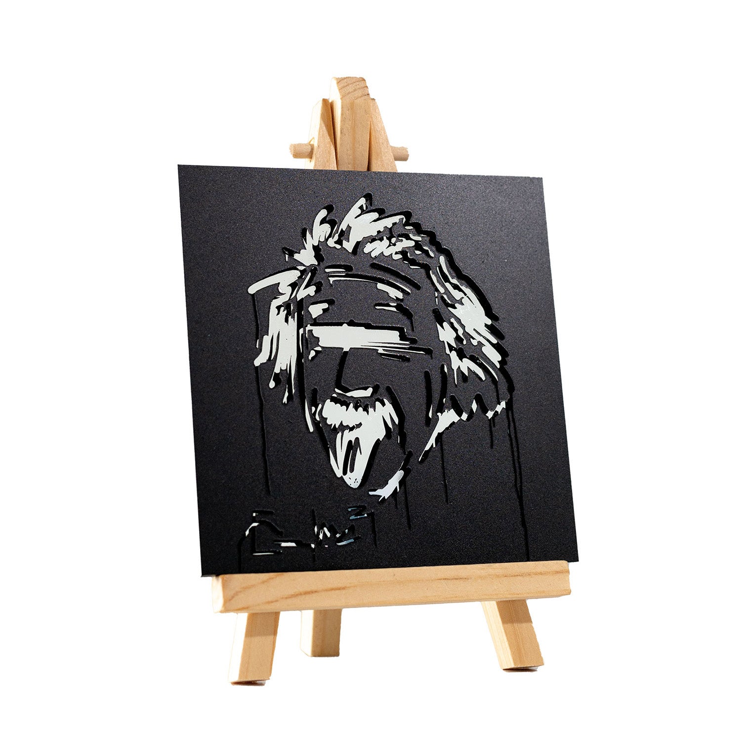 Der Albert Einstein Designspiegel Staffelei zeigt ein lasergeschnittenes Kunstwerk auf einer kleinen Staffelei, das ein stilisiertes, abstraktes Gesicht mit offenem Mund und zerzaustem Haar darstellt und mit scharfen, eckigen Schnitten in Schwarzweiß Street-Art-Vibes aufgreift.