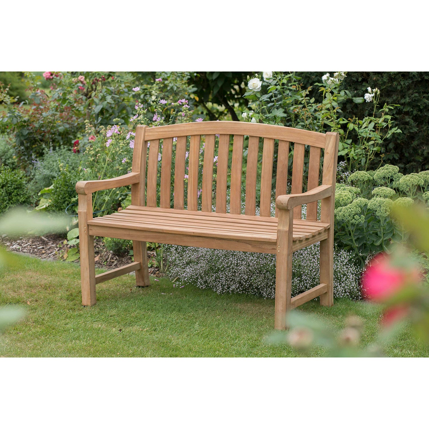 Die Gartenbank aus Holz 2-Sitzer steht auf einer grünen Wiese, umgeben von Pflanzen und Blumen – perfekt für eine stilvolle Gartengestaltung im Freien.