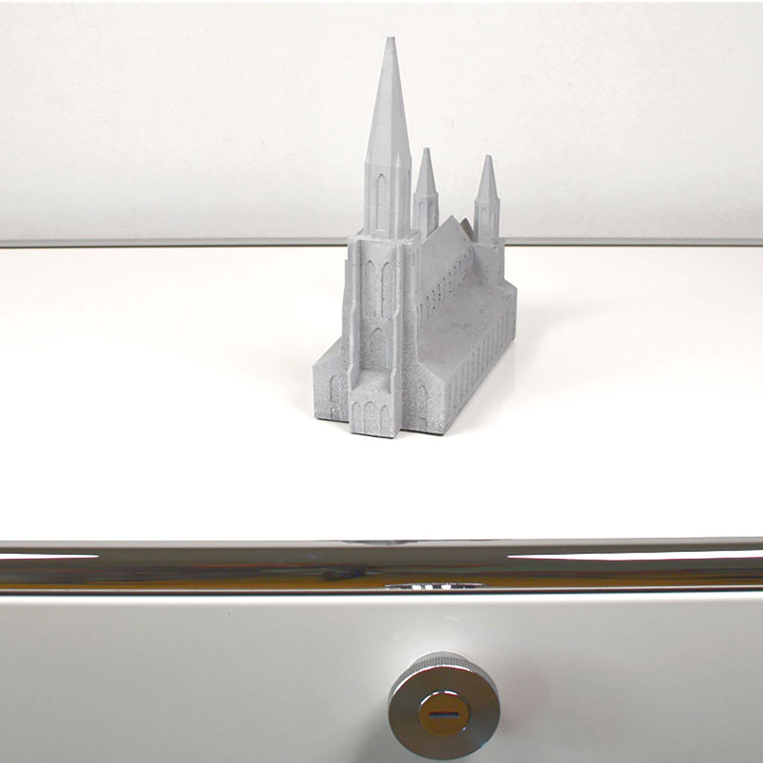 Ein detailreiches Modell aus Ulmer Münster Beton in Graustufen steht auf einer eleganten weißen Kommode. Seine hohe Spitze und die Türme bilden einen schönen Kontrast zum modernen Design mit silbernem Griff und Schloss im Vordergrund.