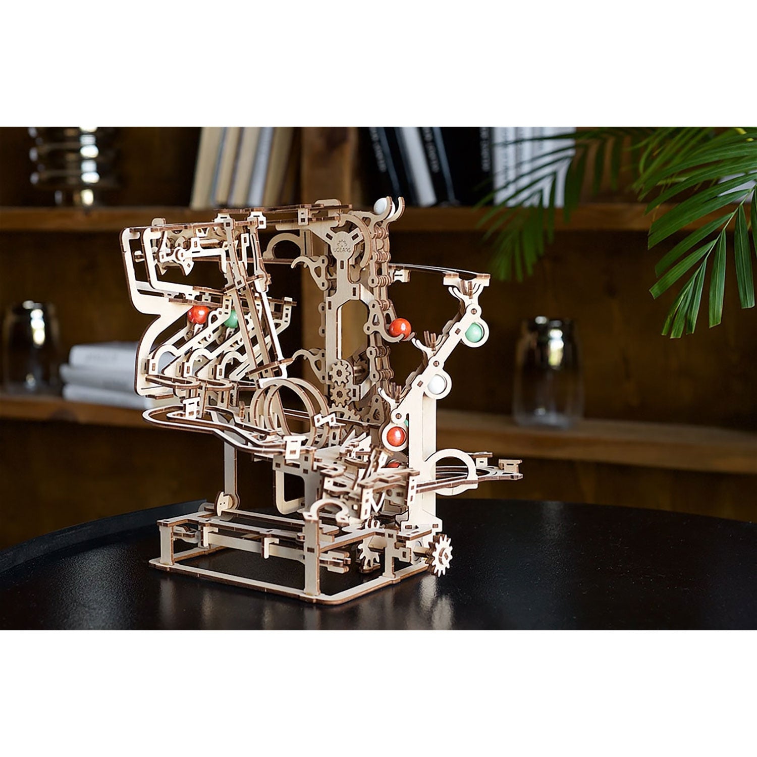 Das 3D-Holzpuzzle „Murmel-Kettenbahn“ ist eine Murmelbahn aus Holz mit komplizierten Zahnrädern und Schienen. Auf einem dunklen Untergrund mit Büchern und einer Pflanze platziert, lädt es die Betrachter in die bezaubernde Welt der Murmelbahnen ein und fängt den Charme eines YouTube-Phänomens ein.