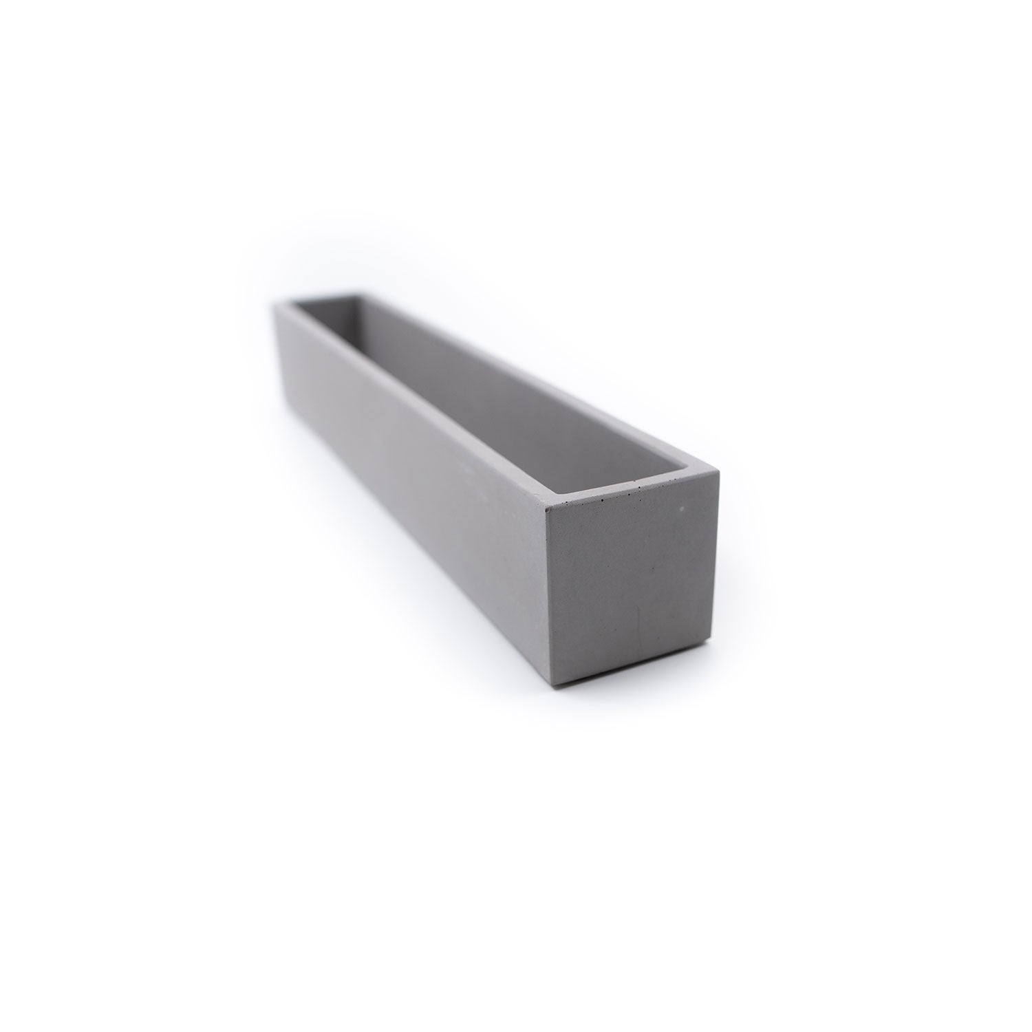 Ein minimalistischer, länglicher, grauer Beton-Blumenkasten, der vor einem schlichten weißen Hintergrund steht. Leer, mit klaren Linien und glatter Oberfläche, verkörpert er stilvolle Pflanzgefäße für jeden modernen Raum.