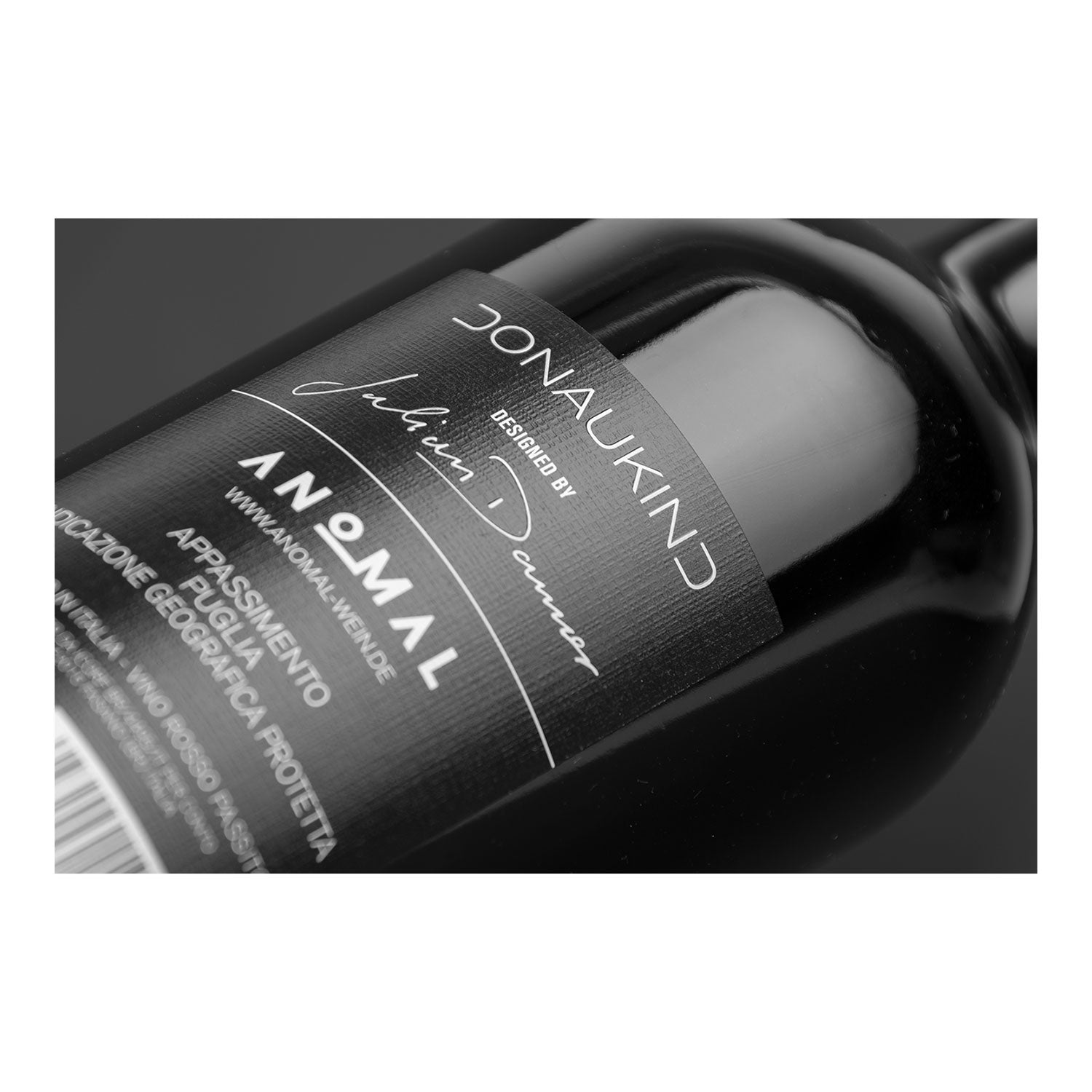 Eine schwarze Weinflasche mit der Aufschrift „Donaukind“ trägt den markanten Schriftzug „Anomaly“ in monochromem Design und verkörpert Julian Danners Anomal-Wein-Handwerk. Diese charakteristische Flasche ist Teil der Premium-Produktion „Appassimento Rosso Puglia“ aus der Linie „3 Flaschen Wein – Zungenbrecher“.