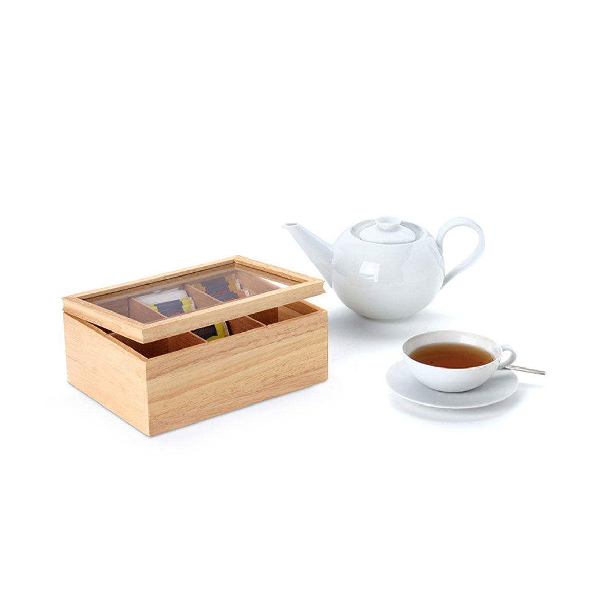 Die Teebeutelbox mit ihrem naturinspirierten Holzdesign und transparentem Deckel enthält neben einer weißen Teekanne und einer Tasse Tee auch verschiedene Teebeutel. Die Tasse auf einer Untertasse mit einem kleinen Löffel steht vor einem schlichten weißen Hintergrund und unterstreicht die natürliche Schönheit des Produkts.